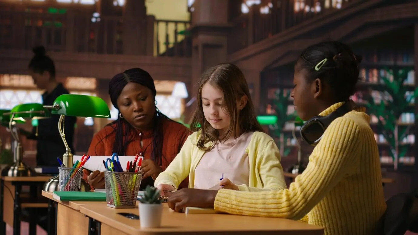 Ergenlik öncesi kızlar ve profesörleri, kütüphanede okul çalışmaları üzerinde işbirliği yapıyor.